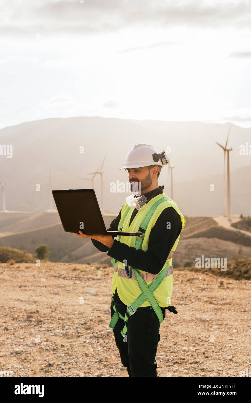 Technician wearing reflective clothing using laptop in front of mountain Stock Photo