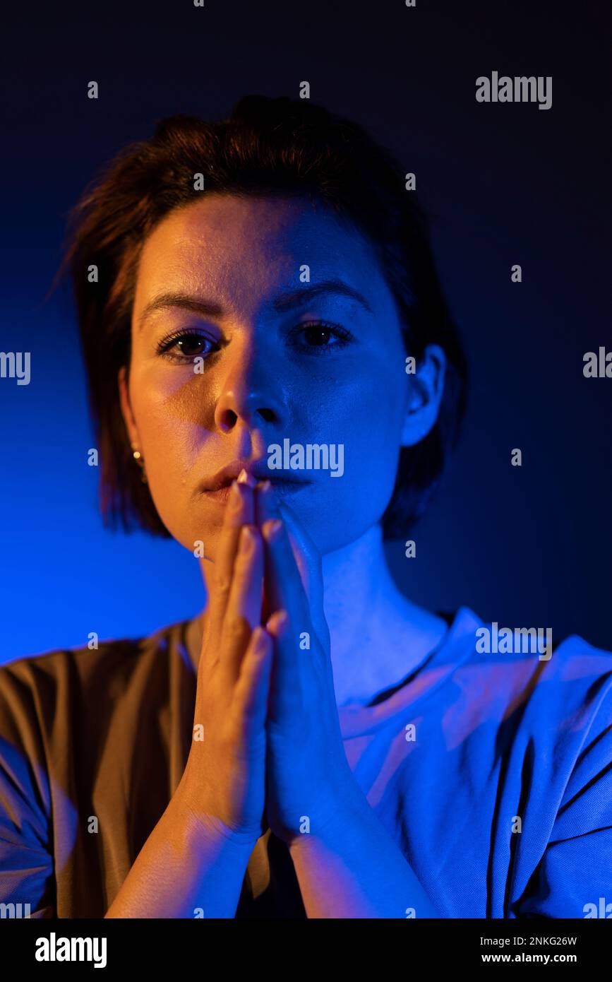 Young woman with blue neon light on face against colored background Stock Photo