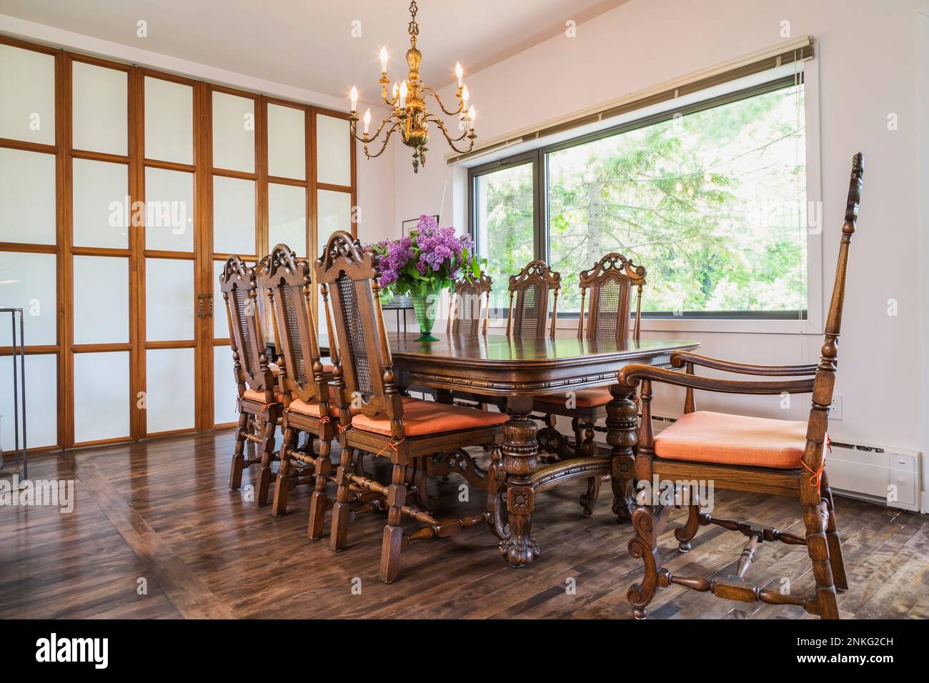 Dining room with 14th century antique wood table and high back grid chairs inside contemporary home. Stock Photo