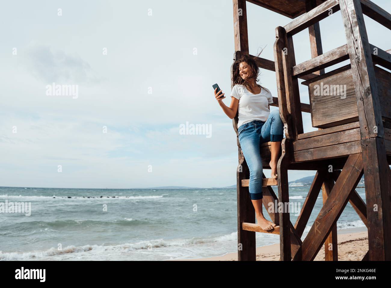 Lifeguard Phone Happy woman using mobile phone sitting on lifeguard hut at beach Stock ...