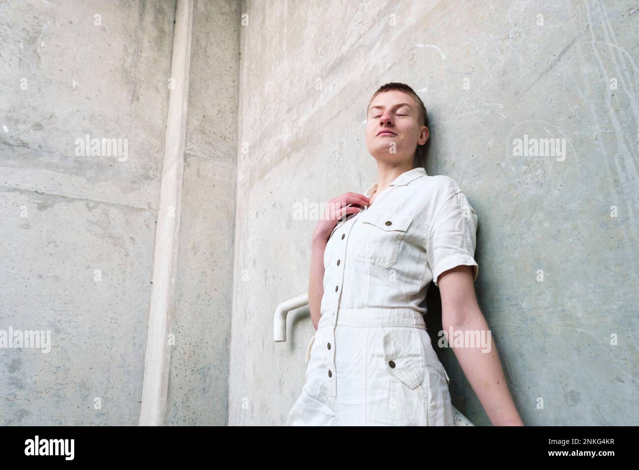 Non-binary person leaning on wall with eyes closed Stock Photo