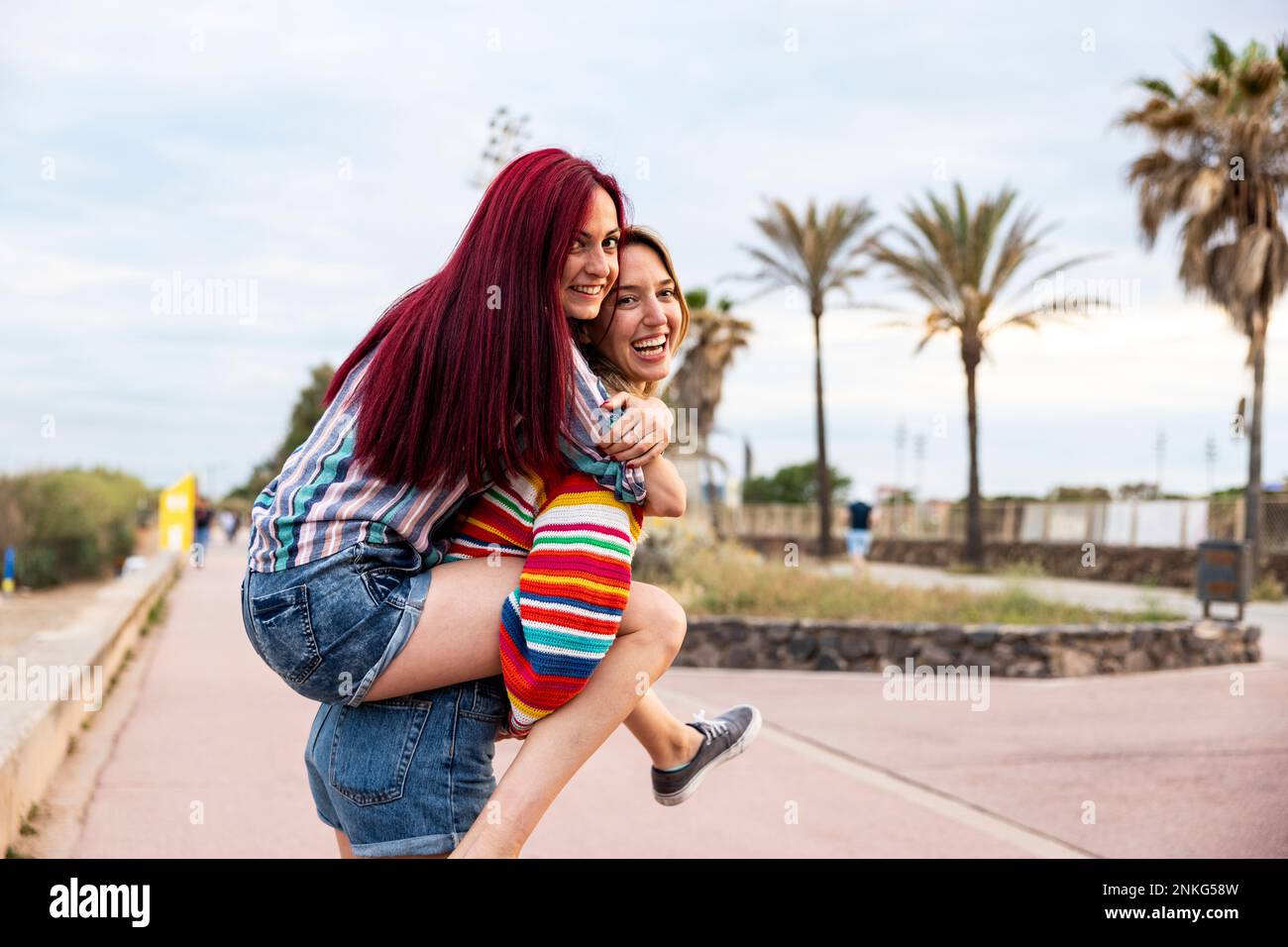 Happy woman giving piggy back ride to friend at promenade Stock Photo