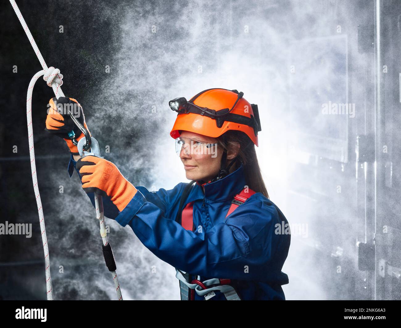 Female industry worker attaching carbiner to climbing rope Stock Photo