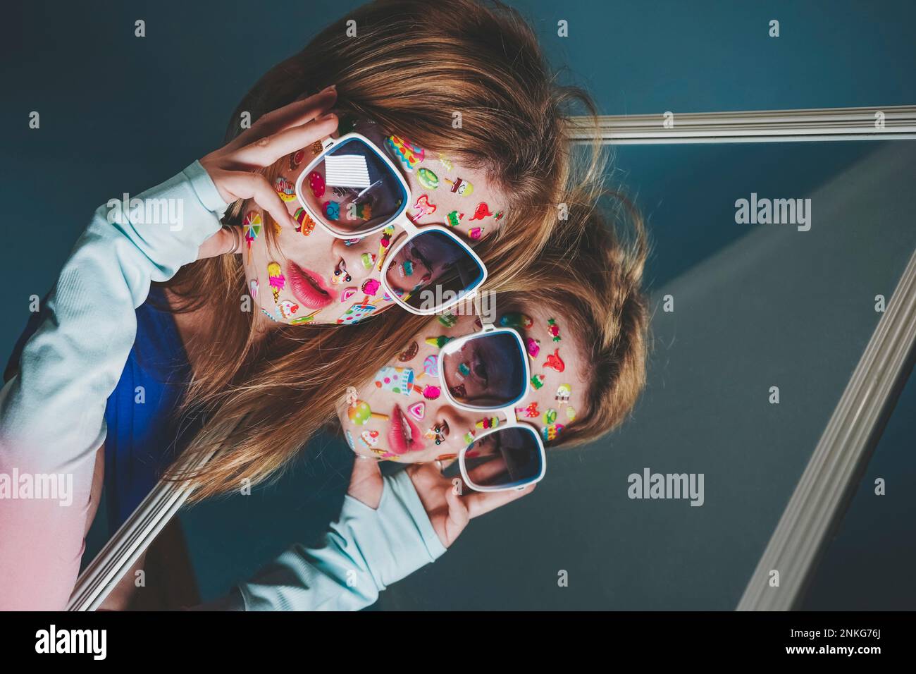 Woman with stickers over face wearing sunglasses and leaning on mirror