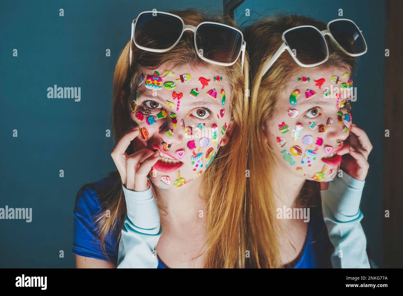 Woman with stickers over face biting fingers against blue background