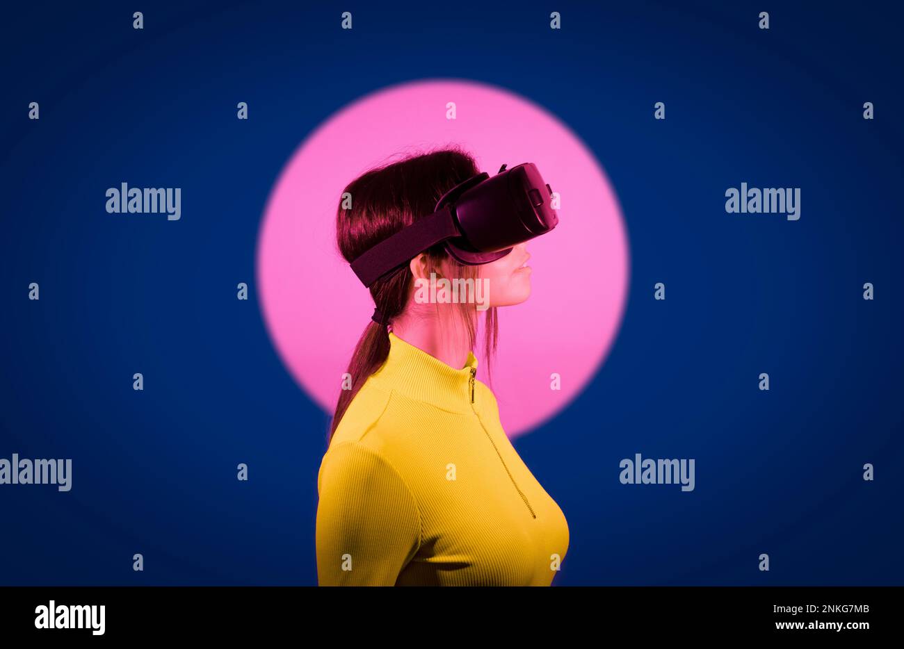 Woman watching on virtual reality goggles by pink light over black background Stock Photo