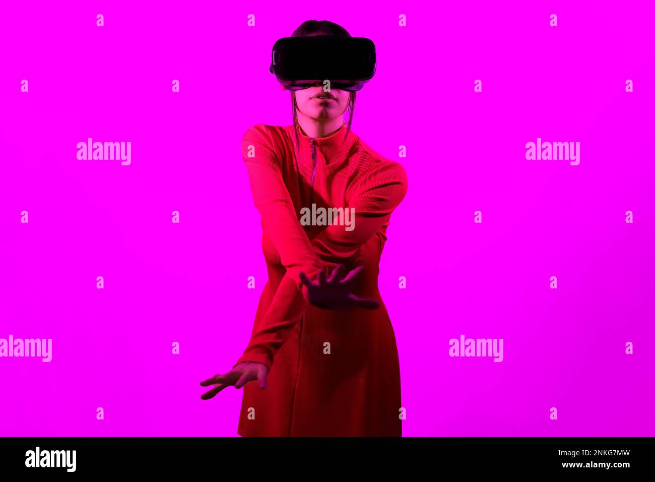 Young woman wearing virtual reality goggles gesturing over pink background Stock Photo