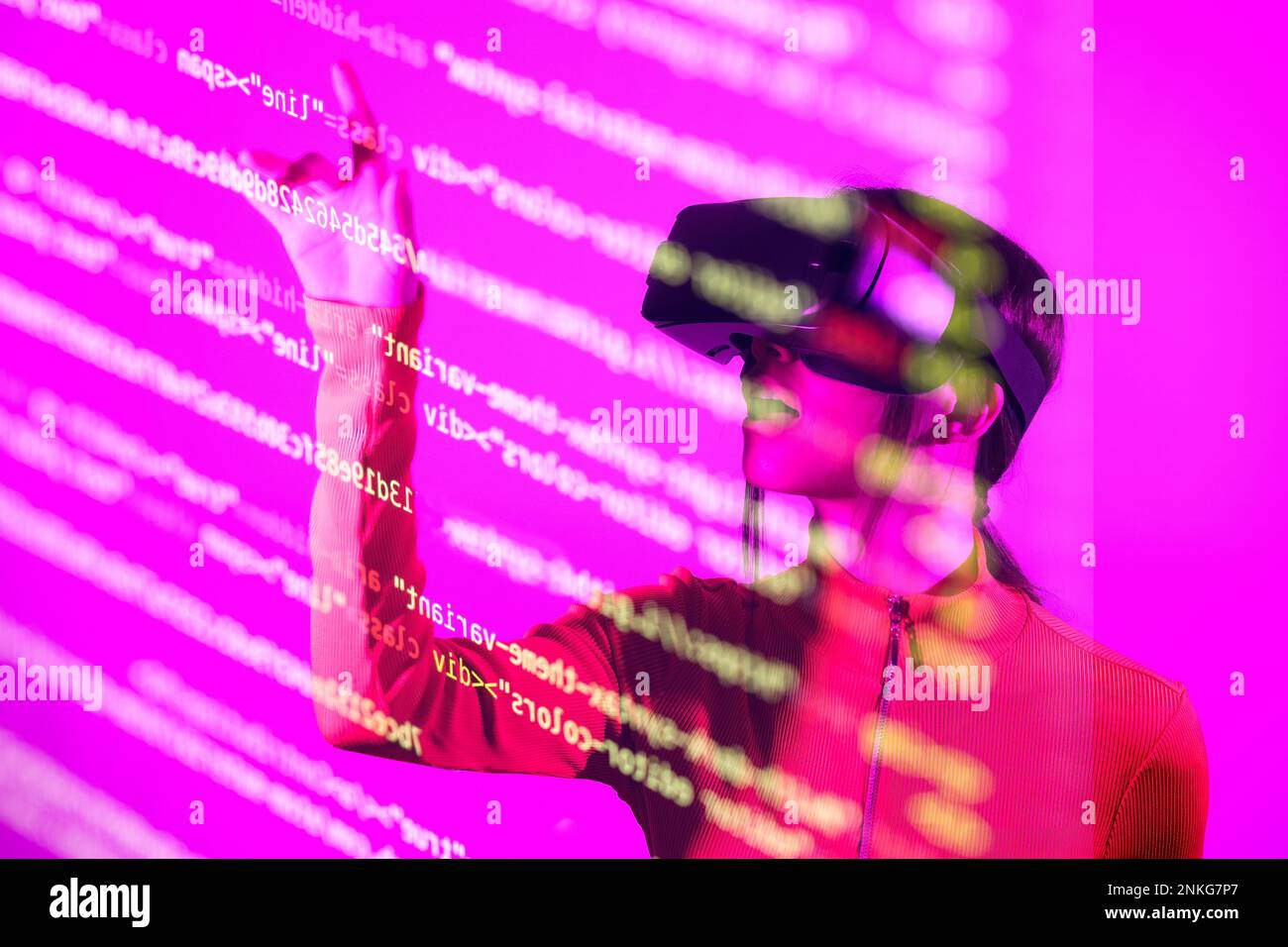 Woman with VR goggles touching computer codes over pink background Stock Photo