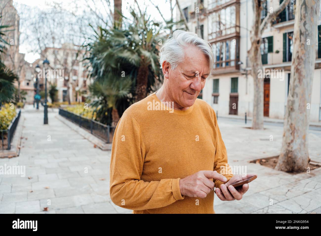 Senior man using smart phone at footpath Stock Photo