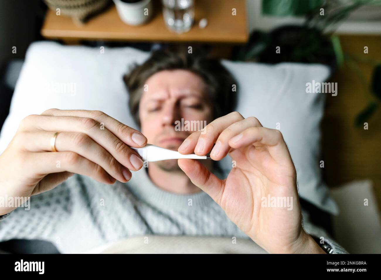 Man looking at thermometer lying on bed at home Stock Photo