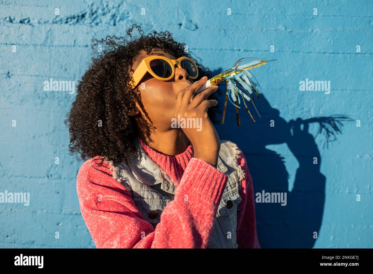 Young woman wearing sunglasses and blowing party horn blower Stock ...