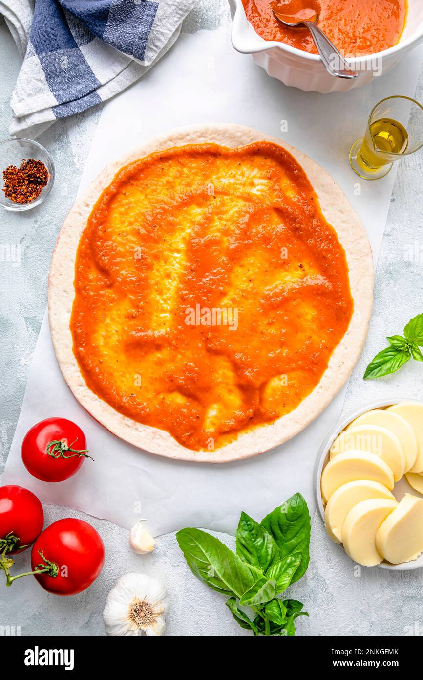 Flay lay of pizza dough with tomato sauce and ingredients kept on table Stock Photo