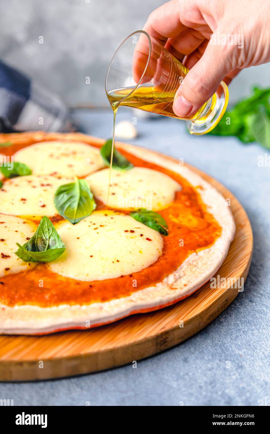 Hand of woman pouring oil on pizza Stock Photo