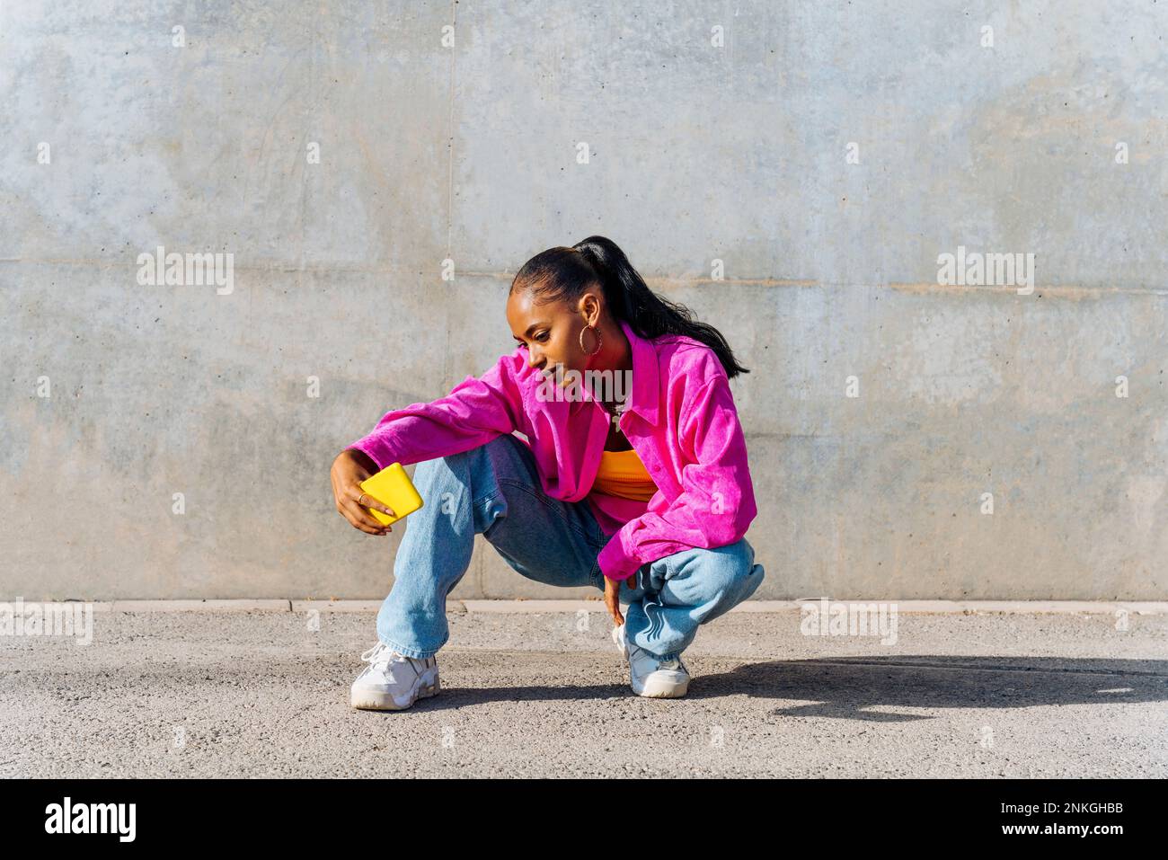 Dancer in squatting position taking selfie through smart phone on sunny day Stock Photo