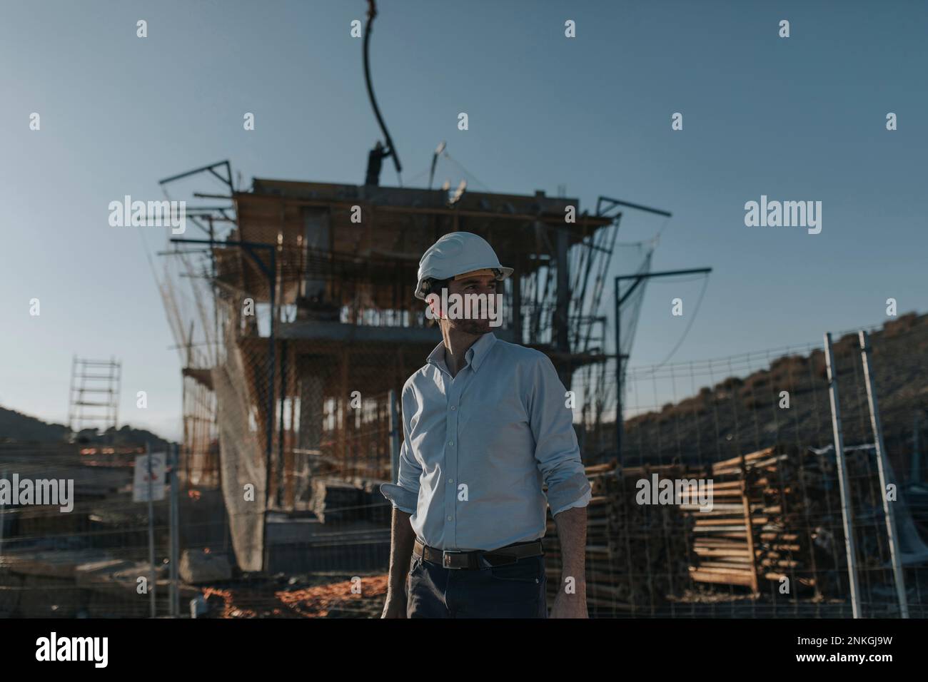 Contemplative architect wearing hardhat standing at construction site Stock Photo