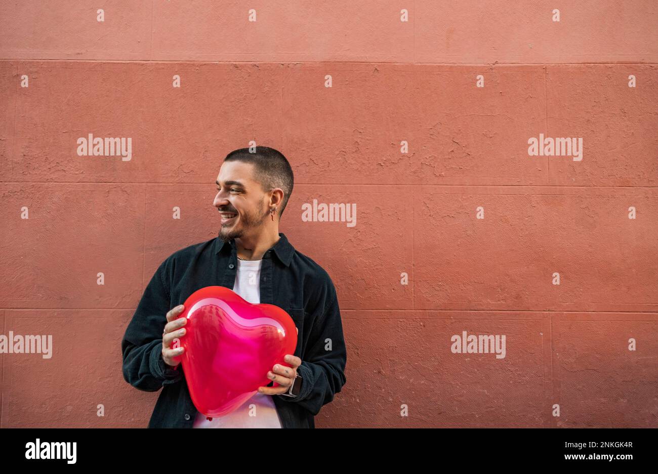 Happy man holding red heart shape balloon in front of wall Stock Photo ...