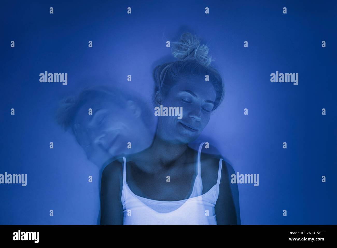 Smiling woman with eyes closed under UV light against blue background Stock Photo