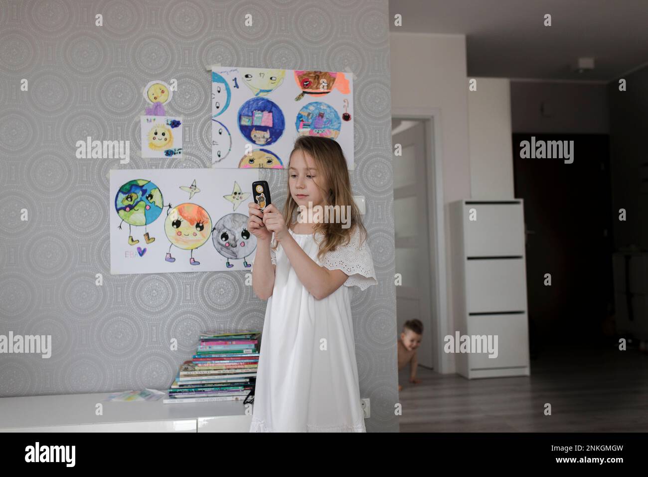 Girl playing with old phone standing by drawings on wall at home Stock Photo