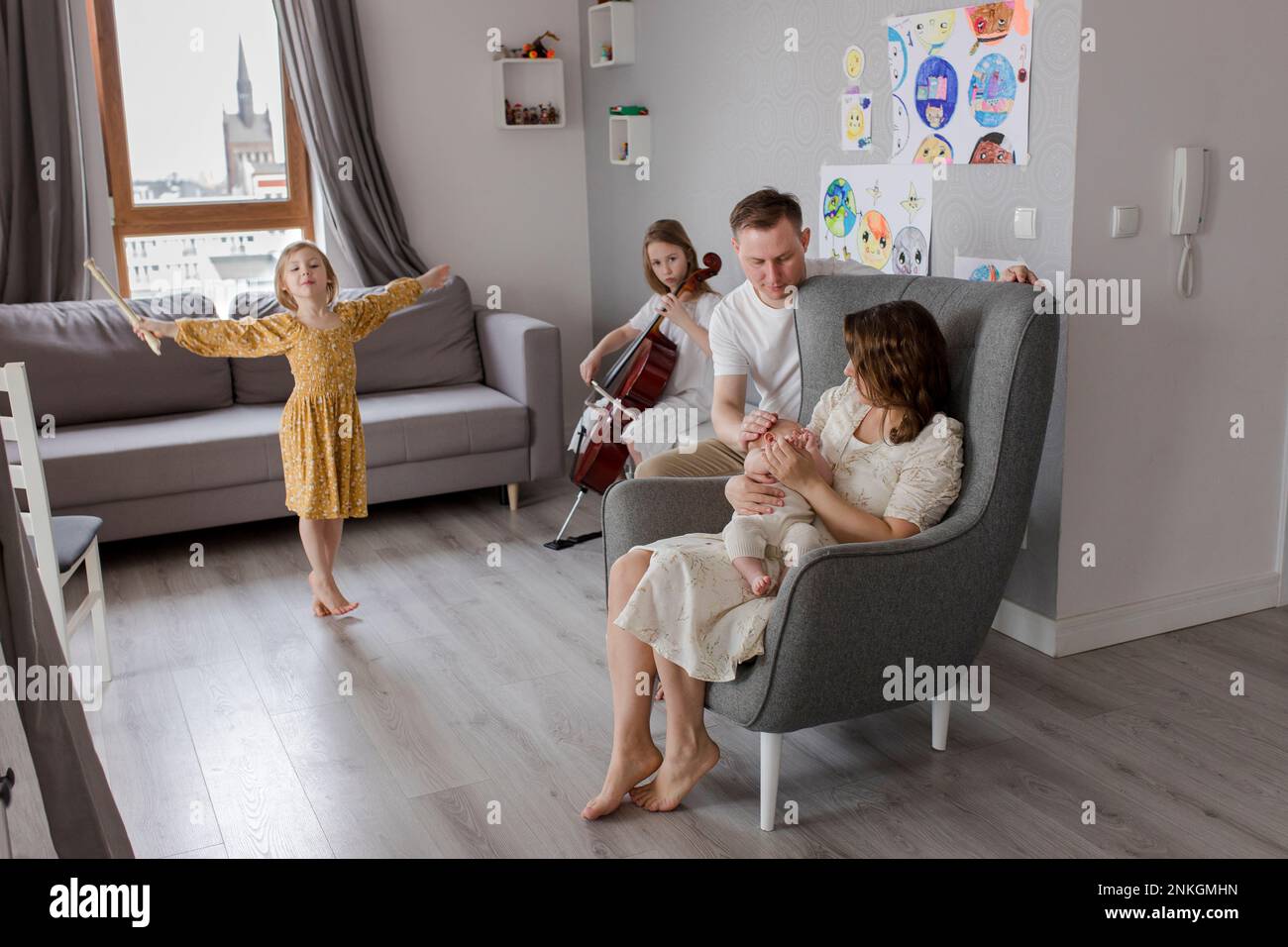 Parents holding baby boy with girls playing musical instrument in background Stock Photo