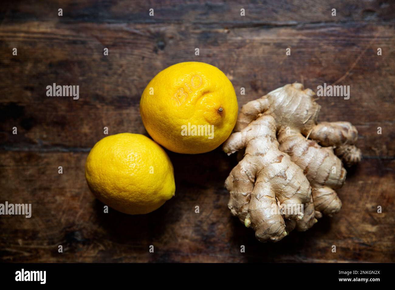 Two fresh lemons and ginger root lying on wooden surface Stock Photo