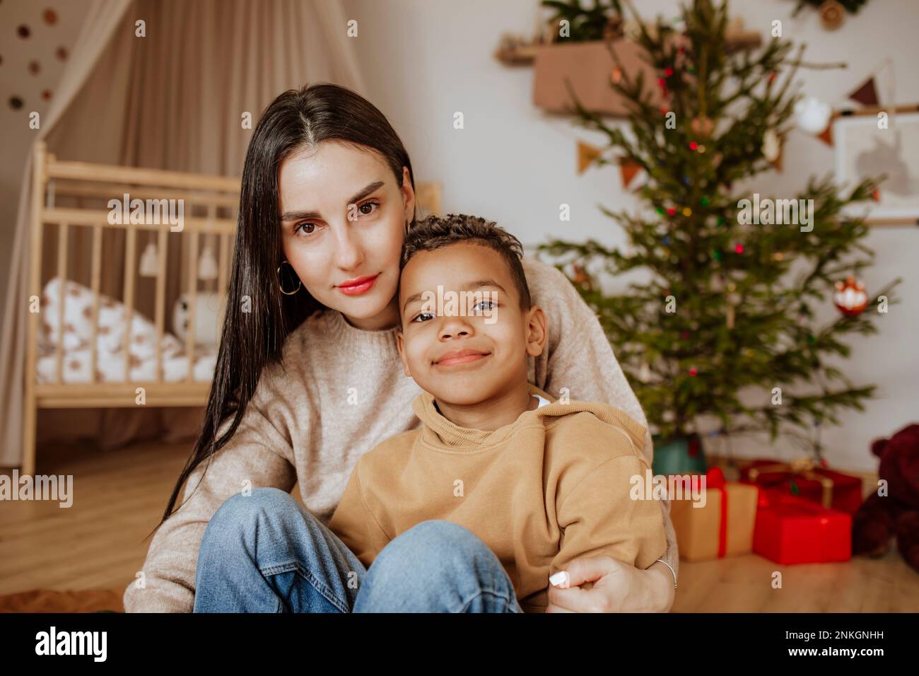 Smiling mother and son sitting in front of Christmas tree at home Stock Photo