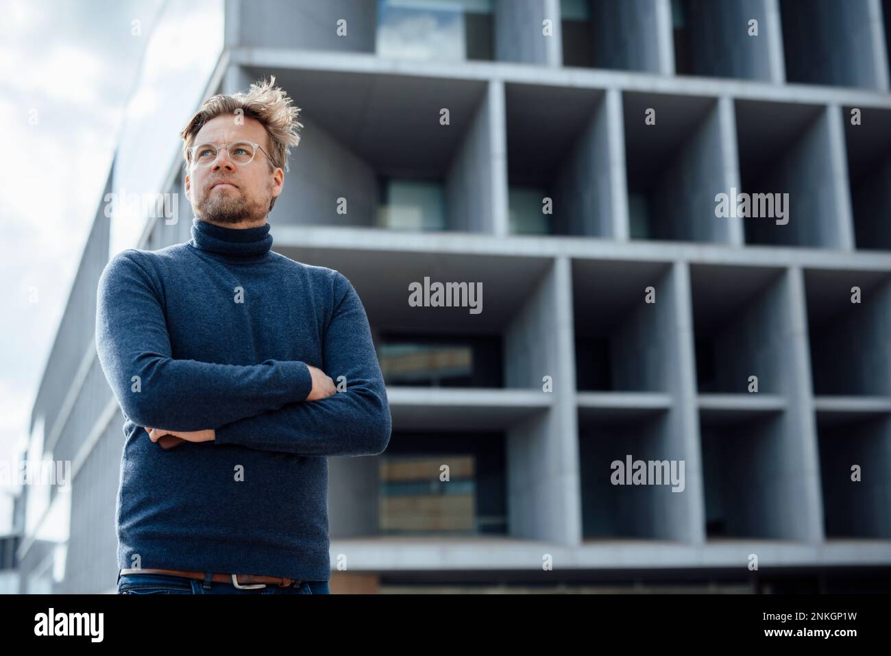 Thoughtful businessman with arms crossed in front of modern office ...