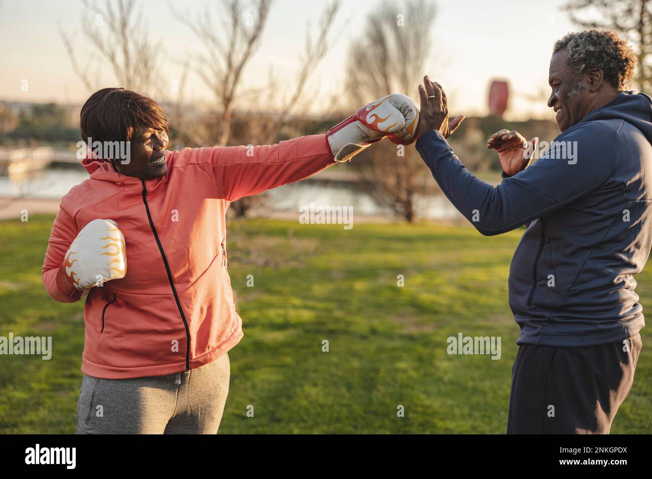 Happy woman wearing boxing gloves punching man at park Stock Photo
