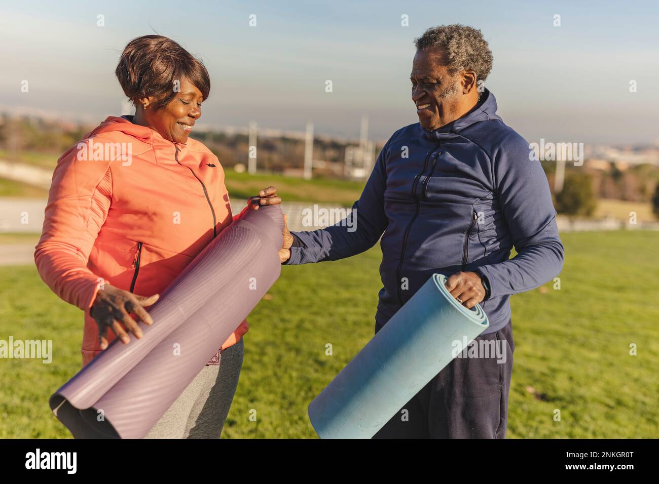 Happy senior woman folding exercise mat with man in park Stock Photo