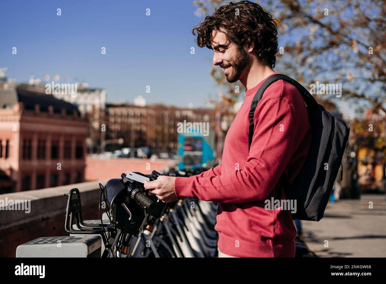 Smiling young man paying with credit card at electric bicycle sharing ...