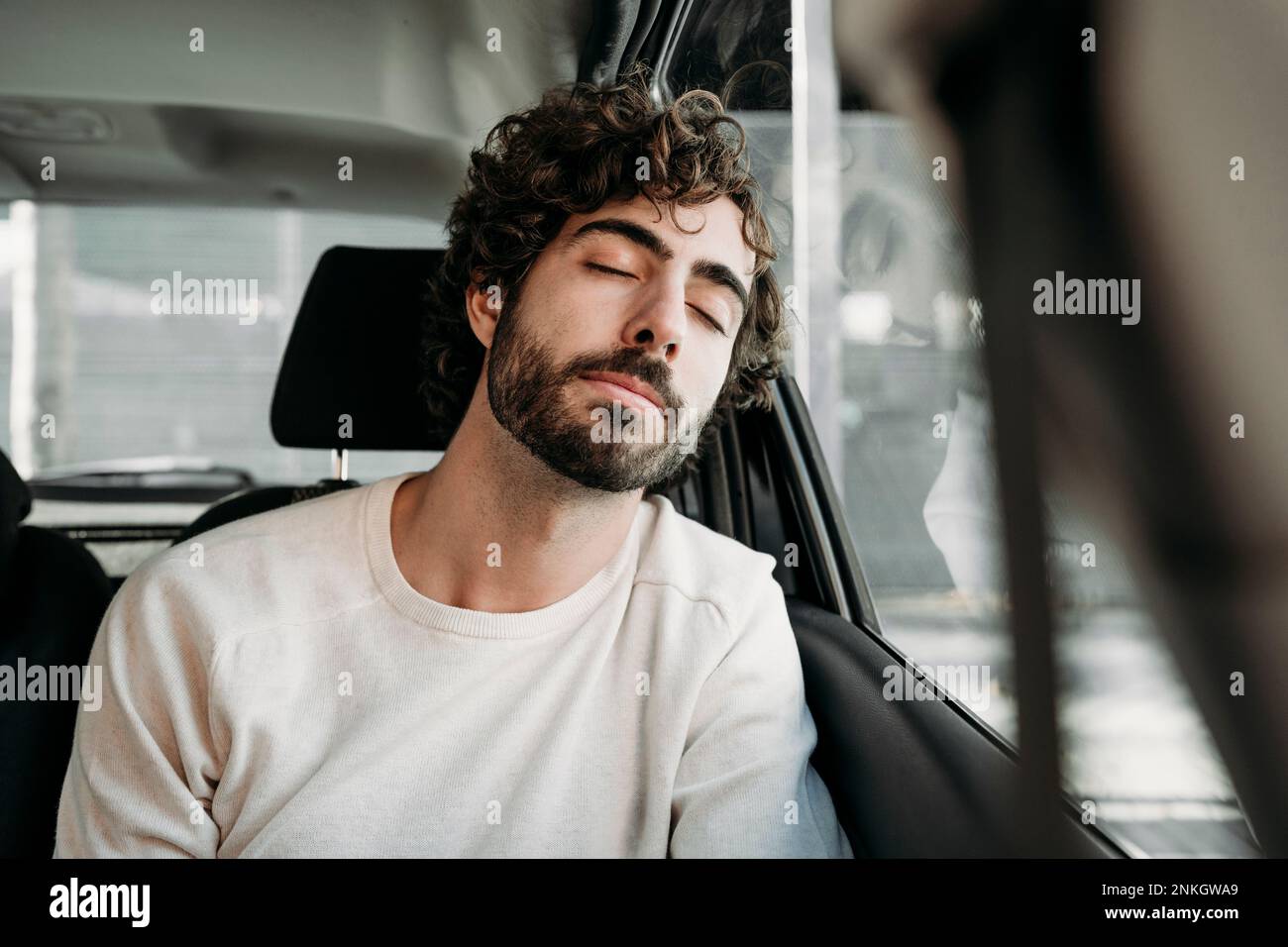 Young man with eyes closed leaning on car window Stock Photo