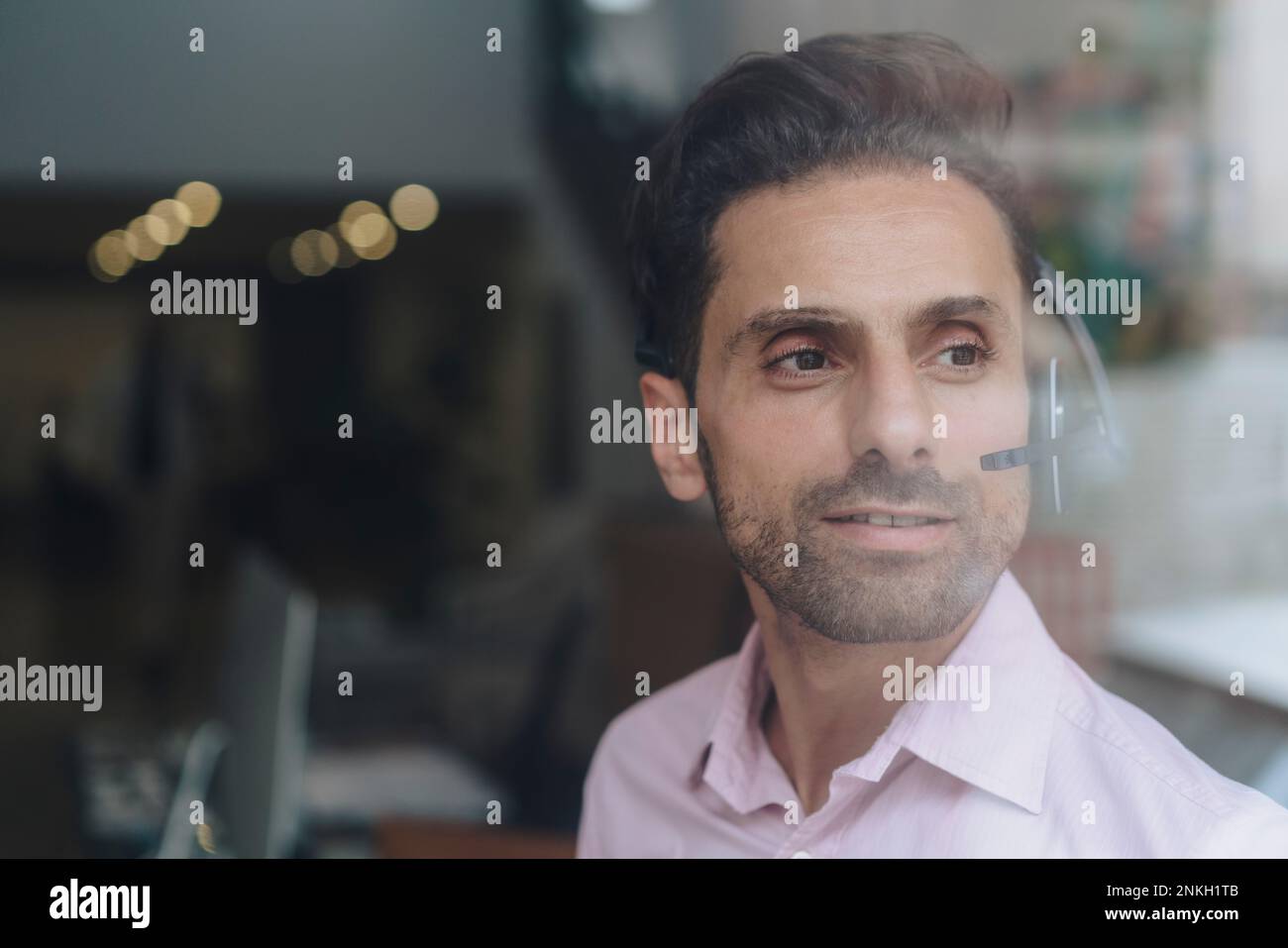 Smiling contemplative businessman wearing headset seen through glass Stock Photo