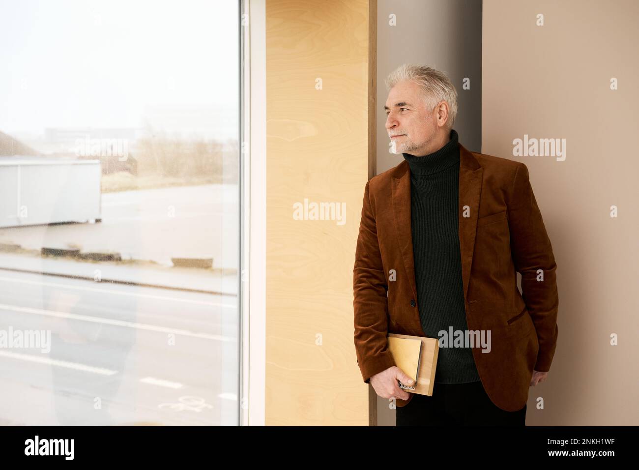 Smiling mature businessman looking through window Stock Photo