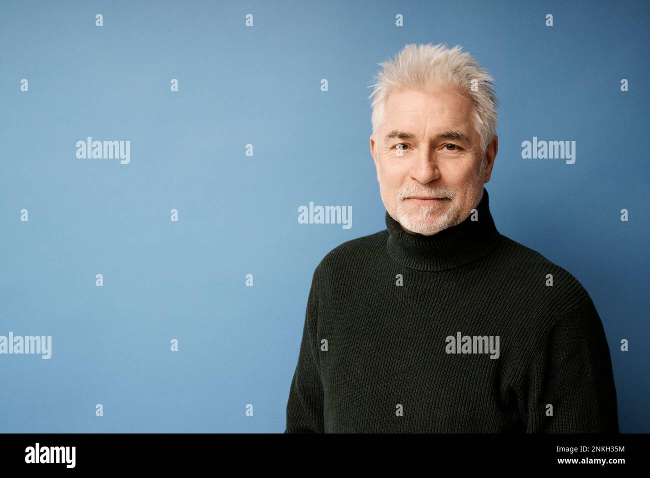 Smiling mature man wearing black turtleneck against blue background Stock Photo