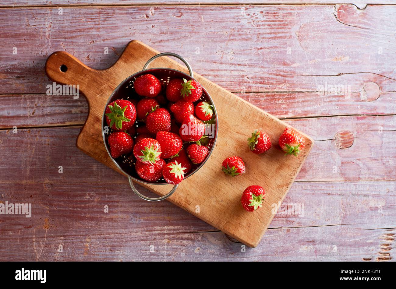 Colander with fresh strawberries lying on cutting board Stock Photo