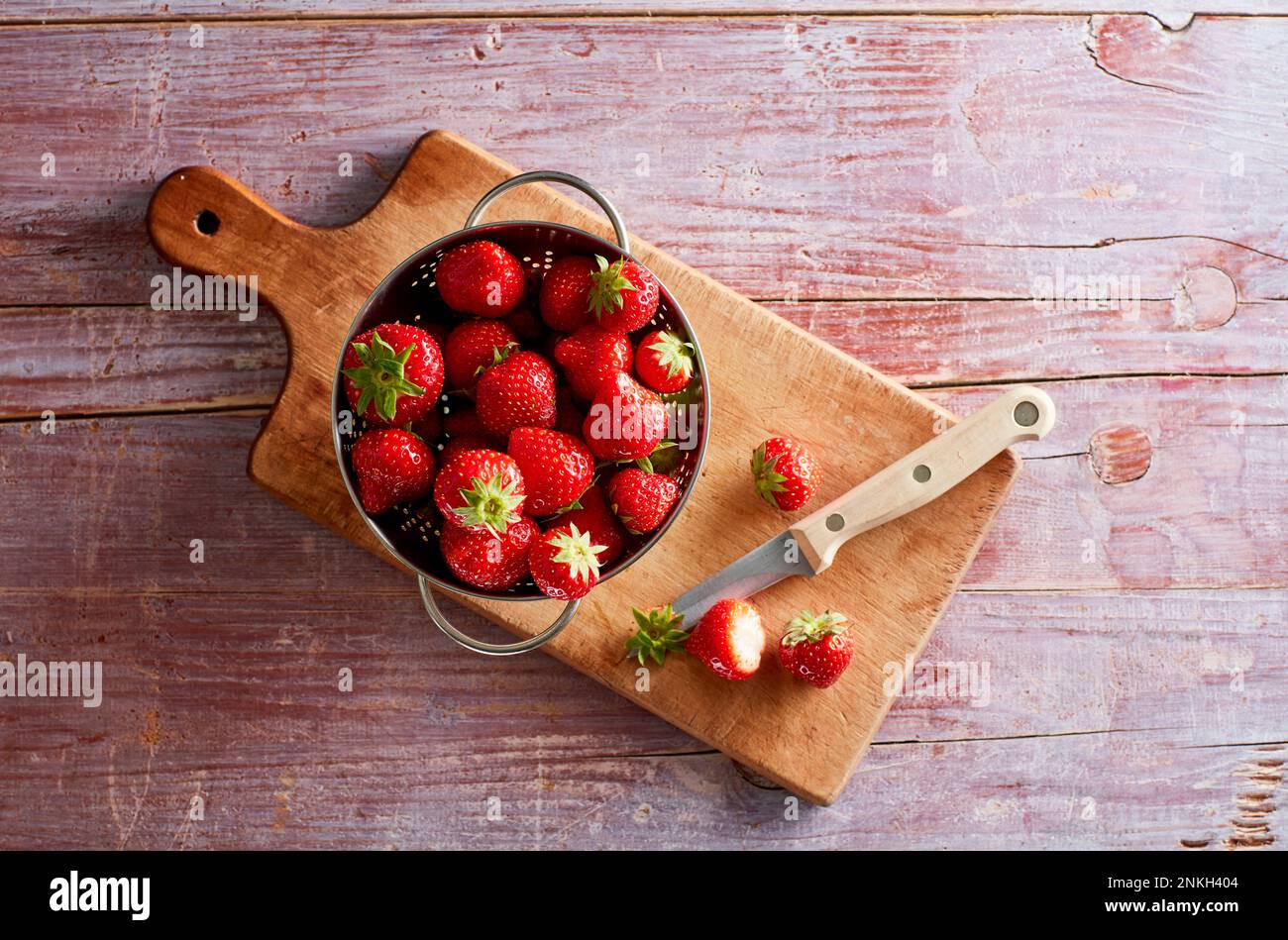 Colander with fresh strawberries lying on cutting board Stock Photo