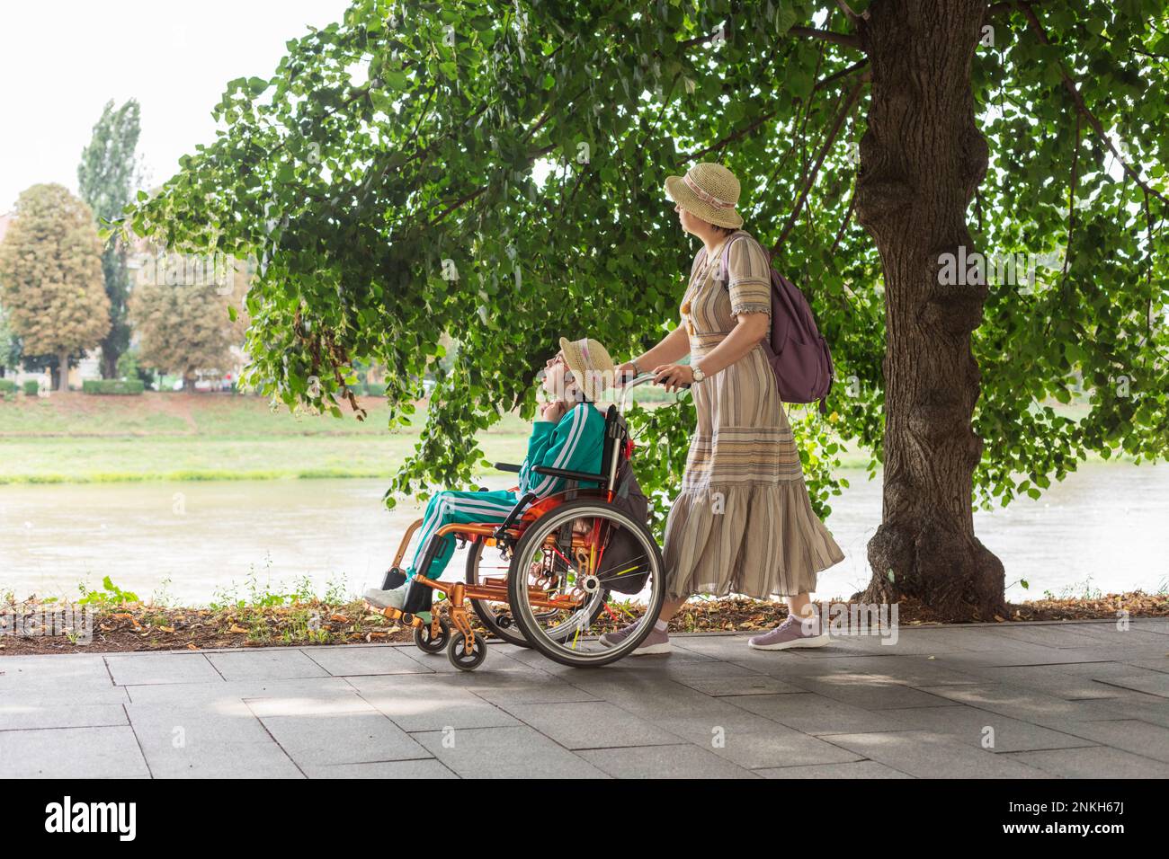 Mother pushing daughter sitting in wheelchair on footpath Stock Photo