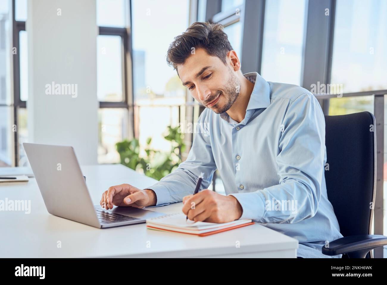 Businessman taking down notes in diary by laptop at office Stock Photo