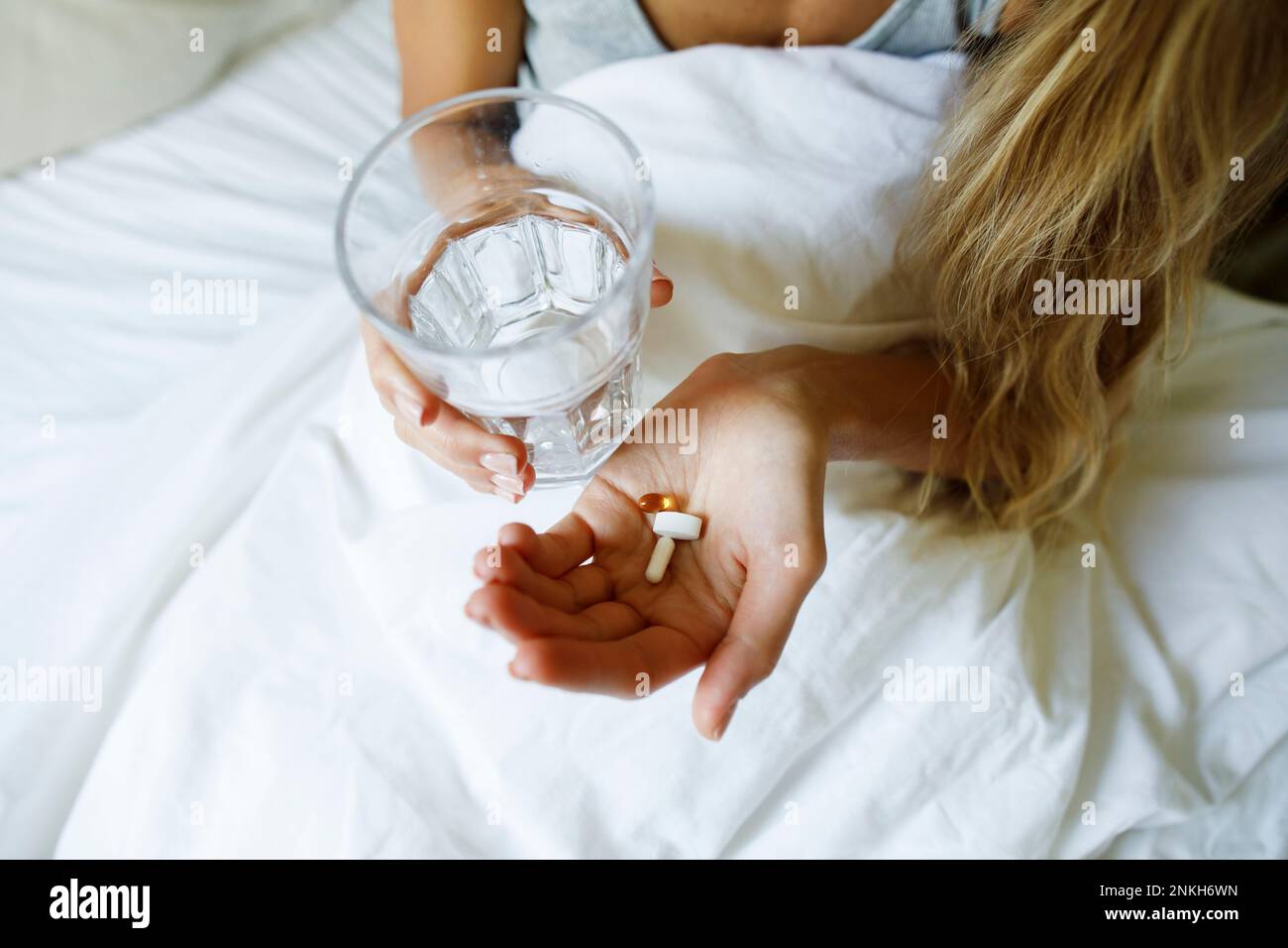 Woman taking pills with glass of water in bed at home Stock Photo