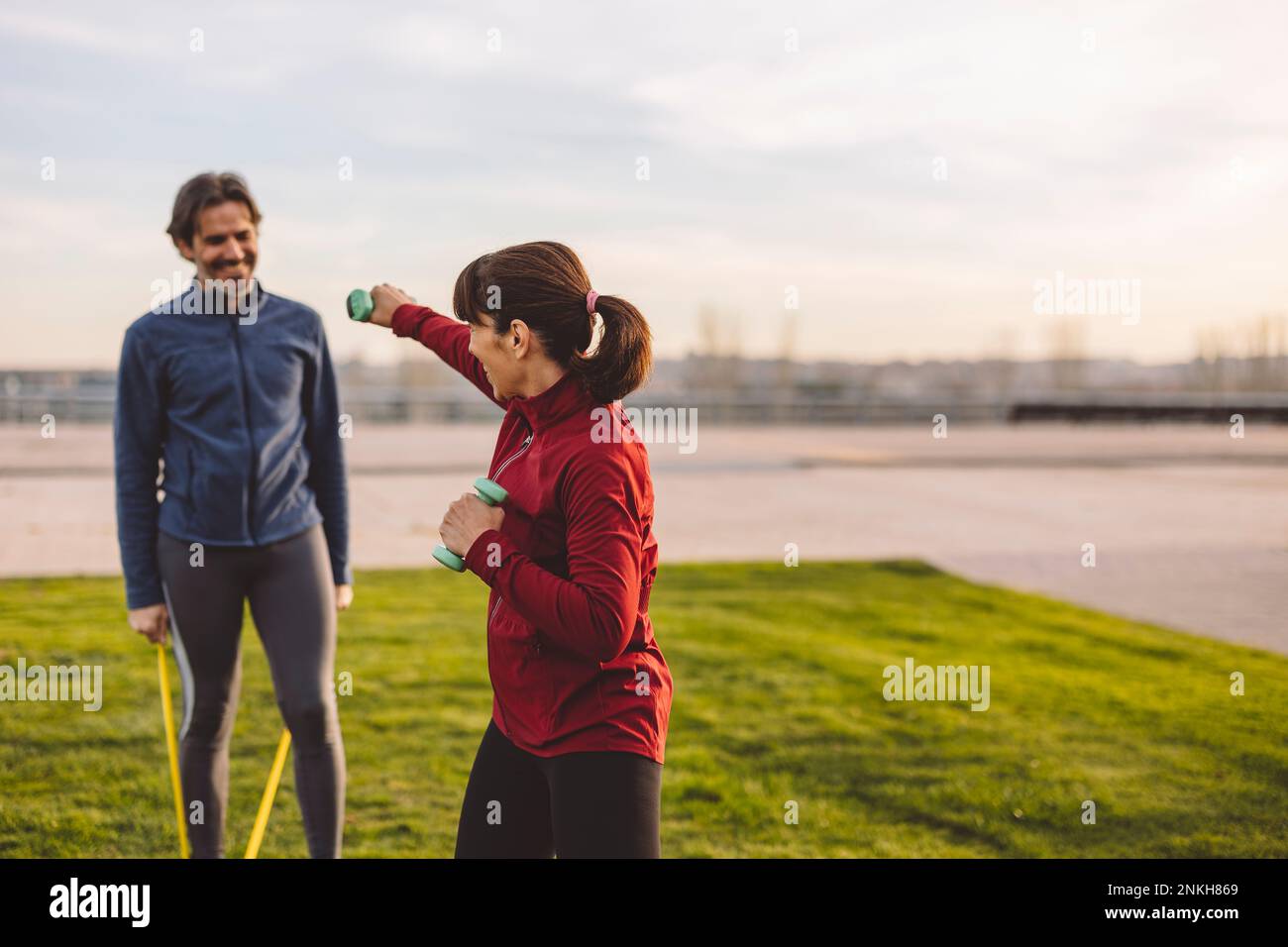 Playful mature woman holding dumbbells exercising with man at park Stock Photo