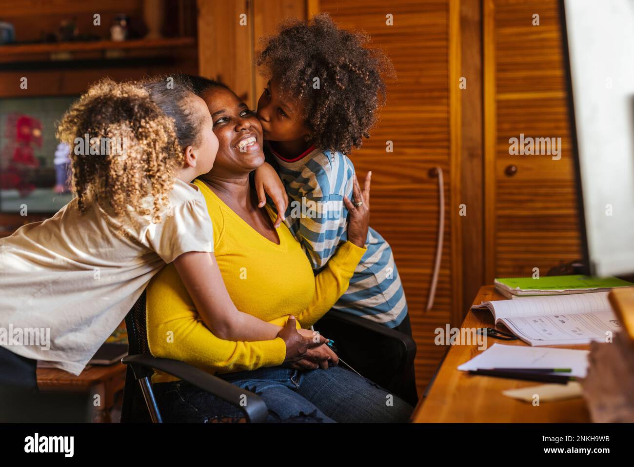 Son and daughter kissing mother sitting at home Stock Photo