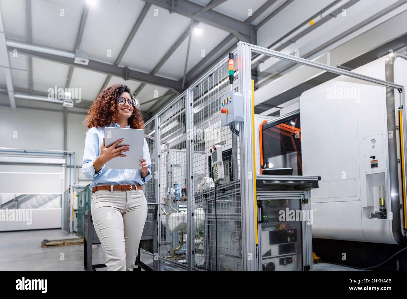 Smiling young engineer standing with tablet PC by machine in industry Stock Photo