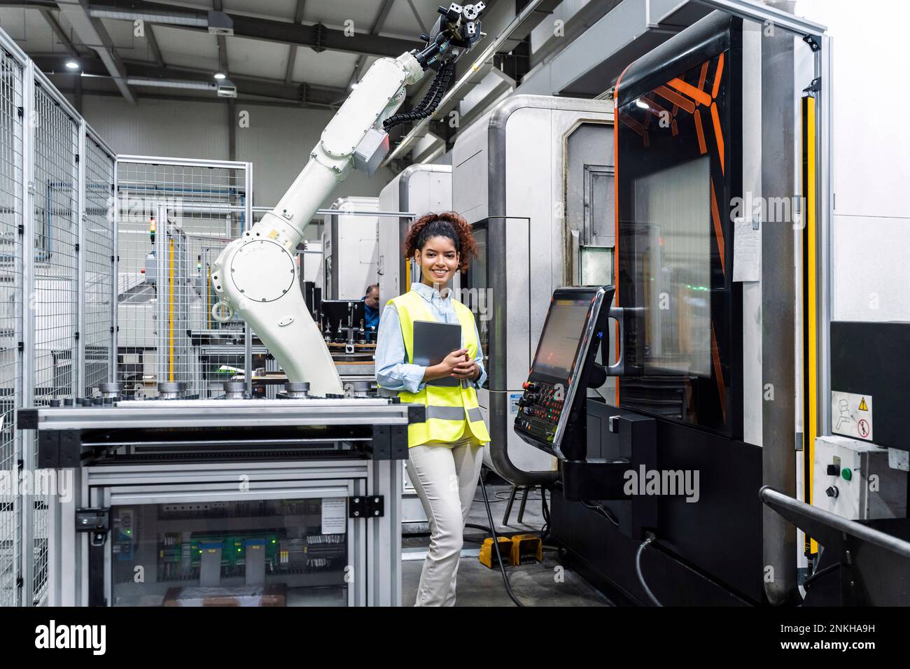 Smiling engineer standing with tablet computer by machine in factory Stock Photo