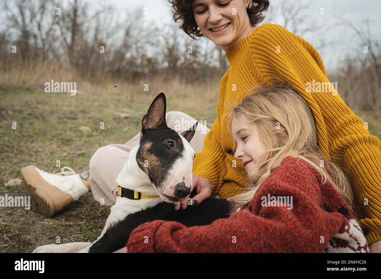 Happy mother and girl sitting with Bull Terrier dog Stock Photo