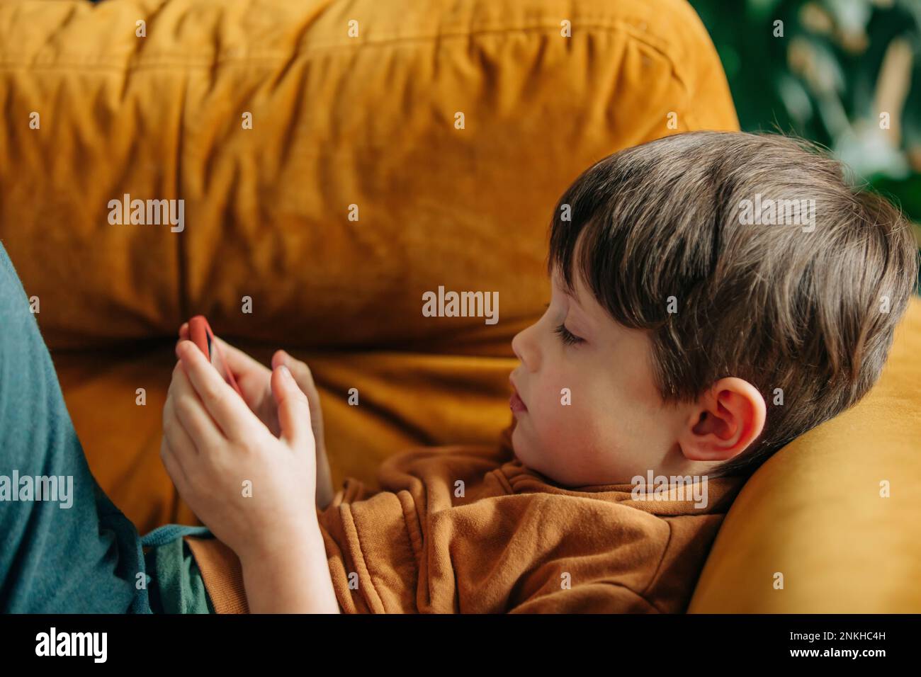 Boy using smart phone lying on sofa at home Stock Photo