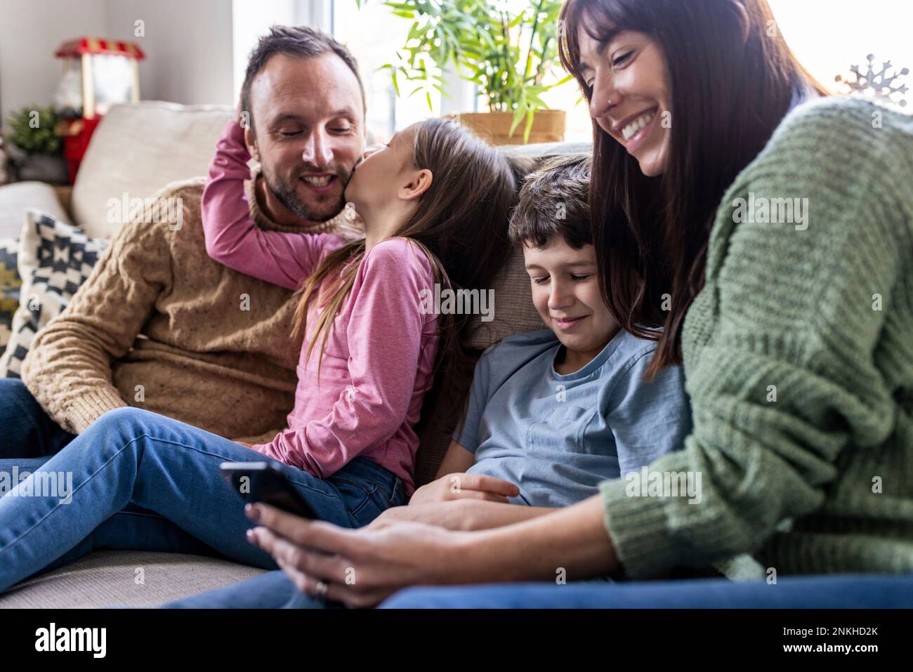 Happy mother using smart phone with son and girl kissing father at home Stock Photo