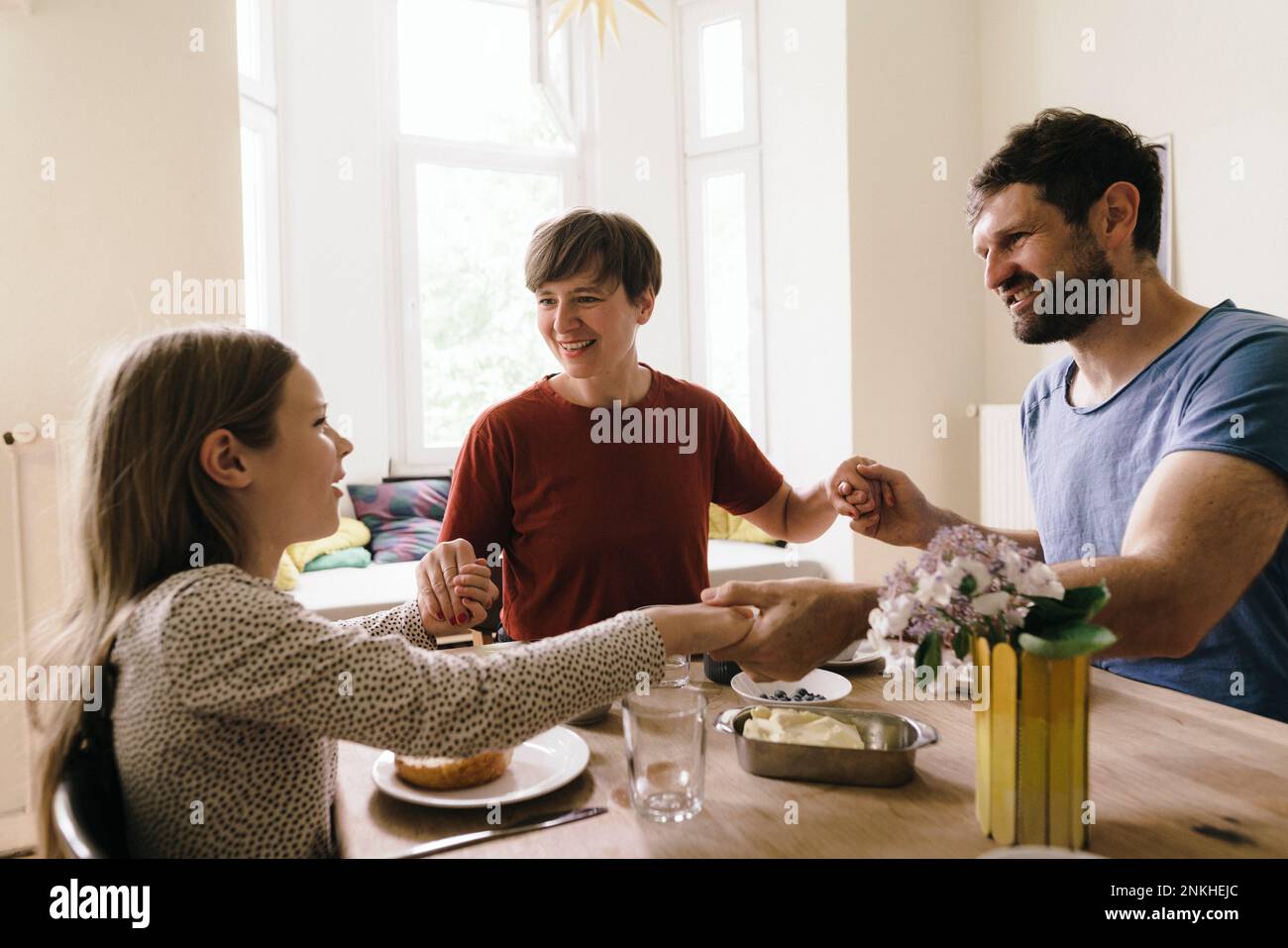 Happy family holding hands sitting at dining table in home Stock Photo