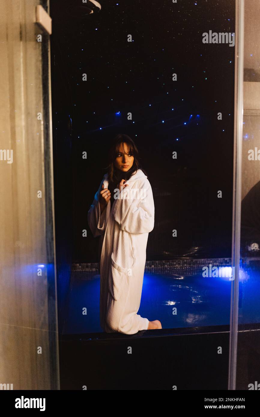 Thoughtful woman wearing bathrobe standing in swimming pool Stock Photo