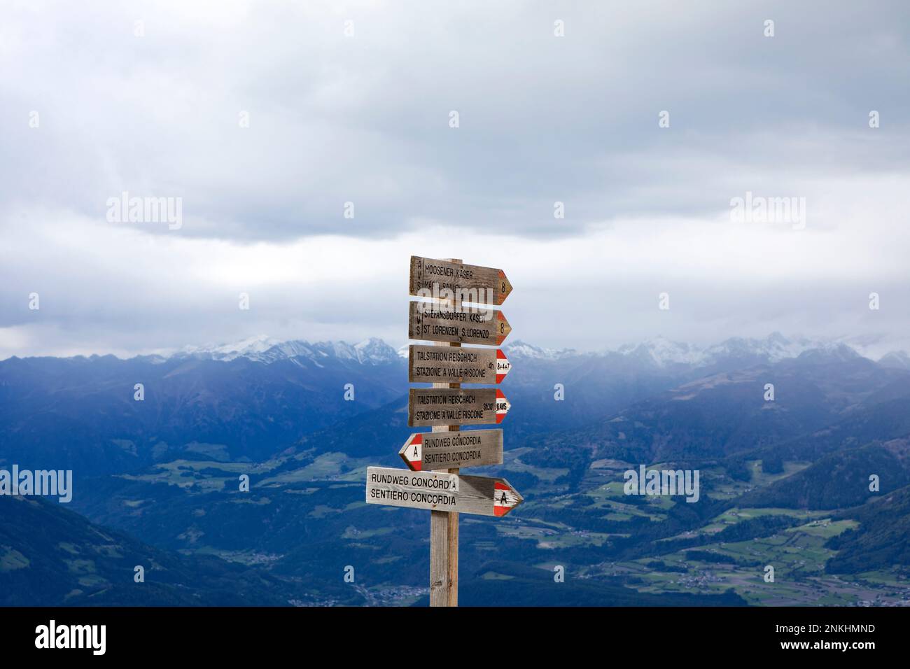 Directional signs by snowcapped mountains under clouds Stock Photo