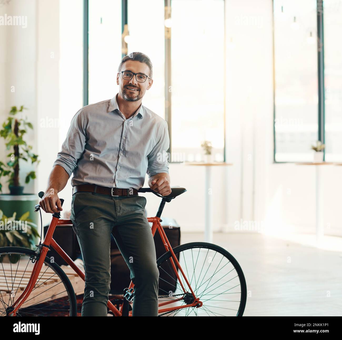 You wont find me late for work using a bicycle. Portrait of a mature businessman standing in a modern office with his bicycle. Stock Photo