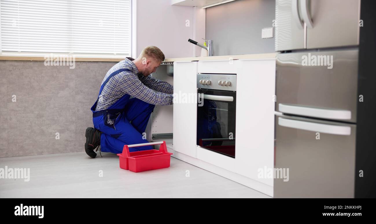 Plumber Cleaning Drain And Pipe In Kitchen Stock Photo